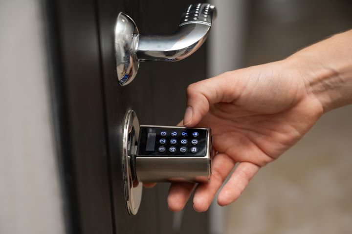 A hand is inputting the code on a digital lock to unlock their front door.