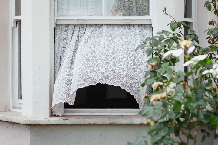an image of a house with its window open, a sheer curtain is blowing out of the open window
